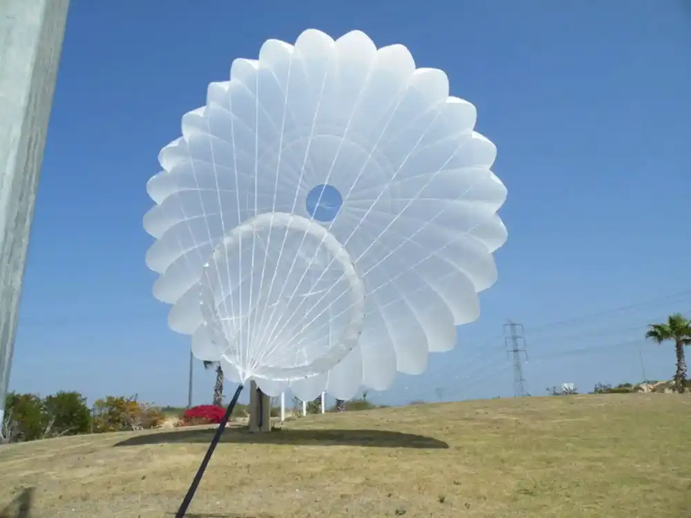 Campana redonda blanca con abertura en el vértice y una segunda campana en su interior, levantada por el viento en el suelo