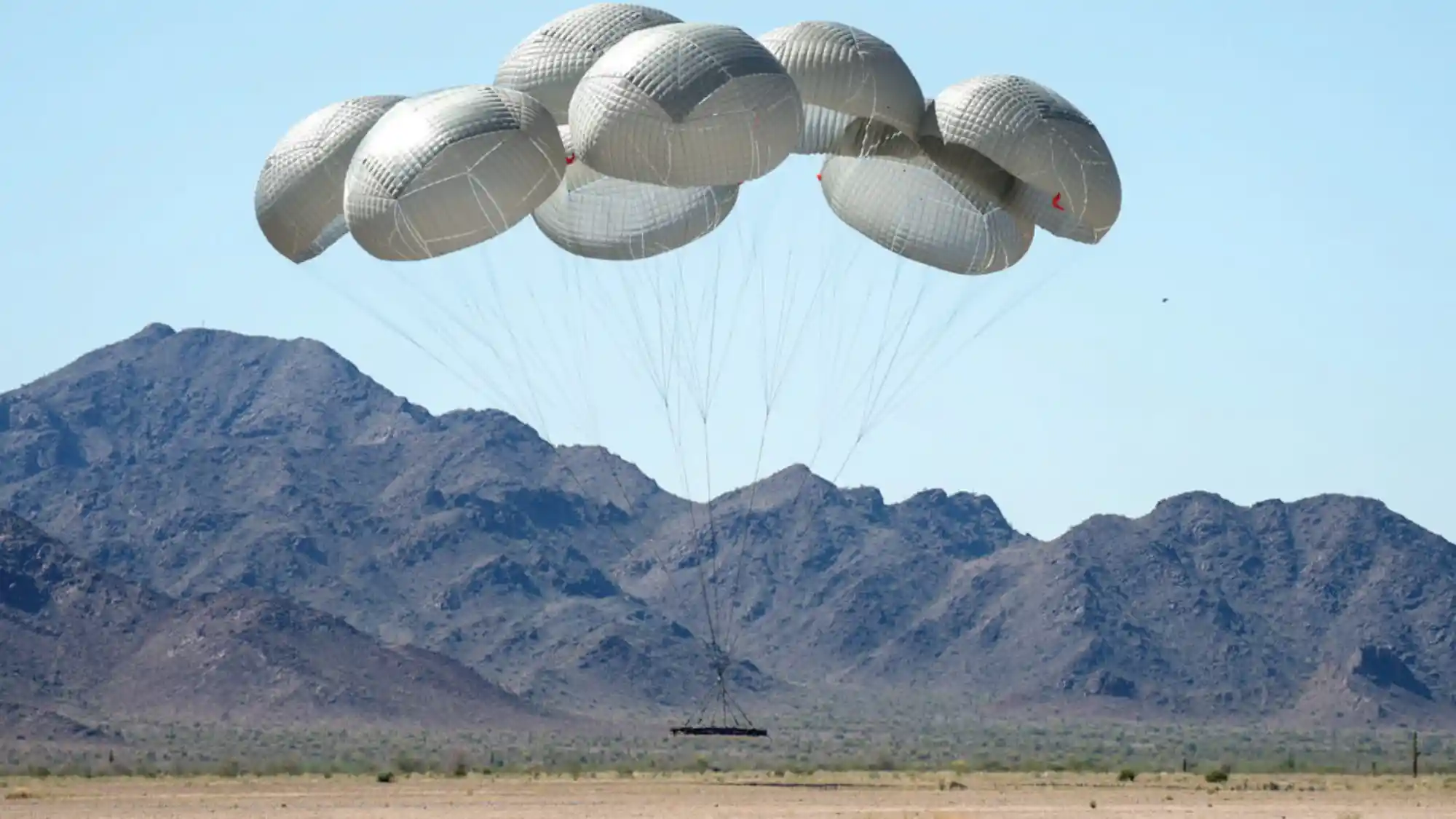 Racimo de varias campanas redondas blancas grandes transportando una carga pesada sobre un desierto con montañas