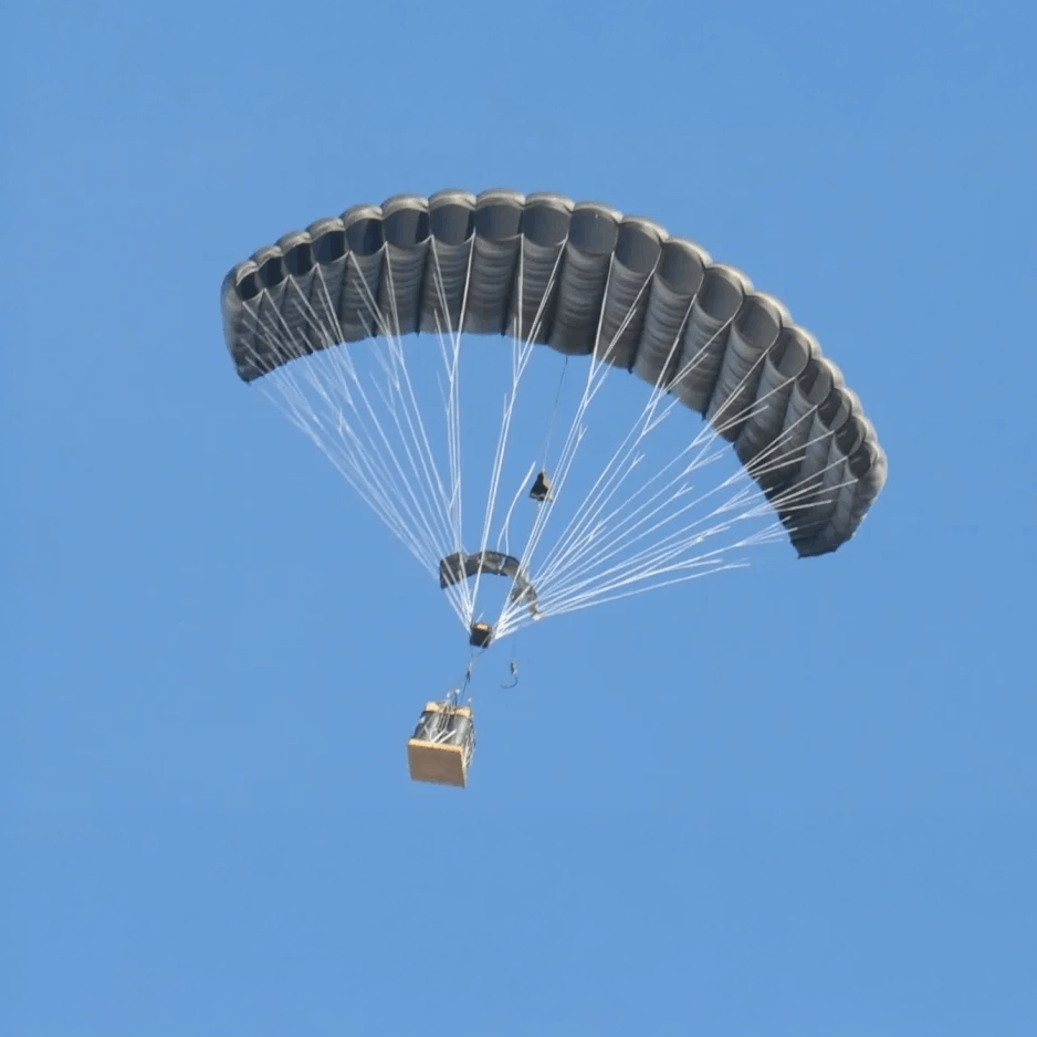 Un solo paracaídas ram-air transportando una carga suspendida en vuelo contra un cielo azul