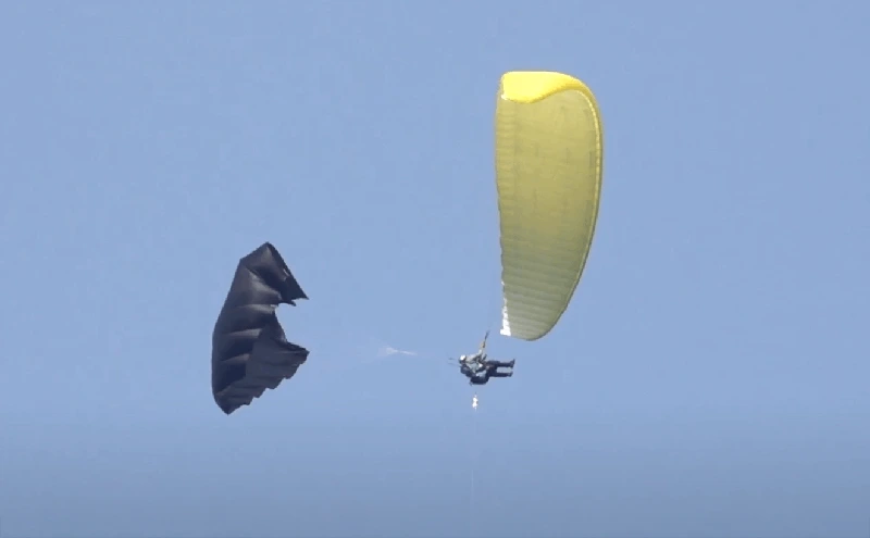 Piloto de parapente que ha lanzado un paracaídas de reserva oscuro, con el parapente amarillo al lado