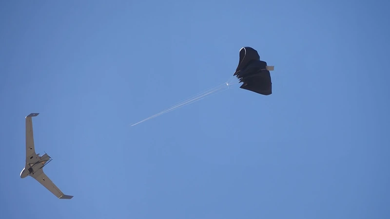 Dron de ala volante en vuelo con el paracaídas de recuperación saliendo por su brida por detrás