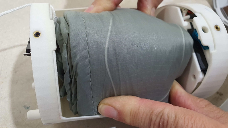 Una mano tiene un contenitore bianco dal quale sporge una velatura grigia ripiegata stretta
