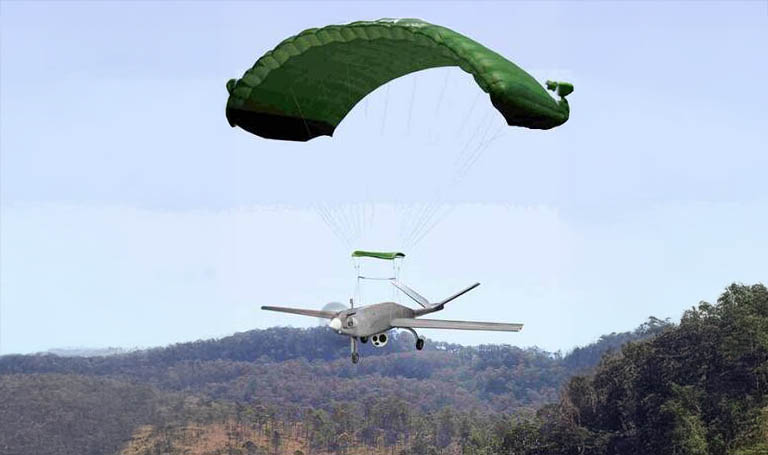 UAV ad ala fissa in discesa sopra colline boscose, con la velatura verde appesa alle funi sopra la fusoliera e la sacca posata in cima