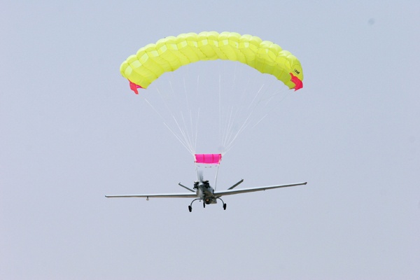 Dron de ala fija bajo un paracaídas ram-air amarillo con slider rosa en vuelo