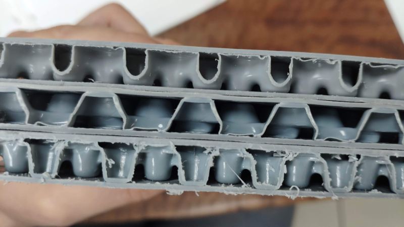 Sección de un absorbedor de impacto de plástico gris multicapa con estructura celular, sostenido en una mano