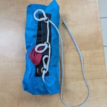Paracaídas anular plegado en una bolsa de despliegue azul con un cordino sobre una mesa
