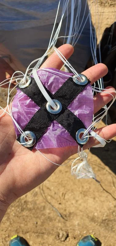 Piccolo slider in tessuto viola con una croce di fettuccia e occhielli metallici attraverso i quali passano le funi