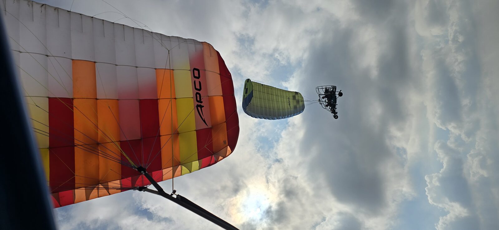 Vista desde debajo de una vela hacia un segundo trike que vuela por debajo contra un cielo nublado