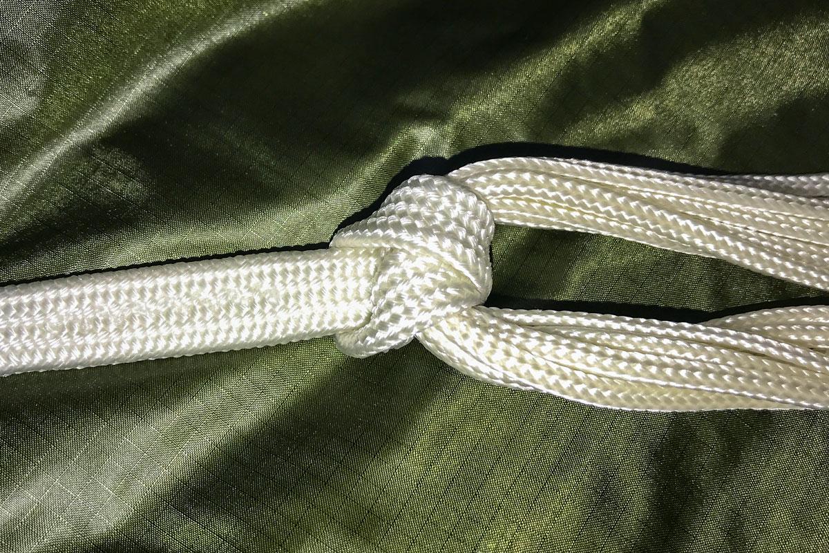 Primer plano de una suspente blanca trenzada anudada en su punto de anclaje sobre tela de campana verde oliva