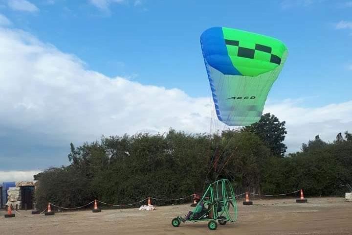 Trike sobre una franja de arena balizada con conos, con su vela verde y azul elevándose en diagonal sobre la máquina por las suspentes