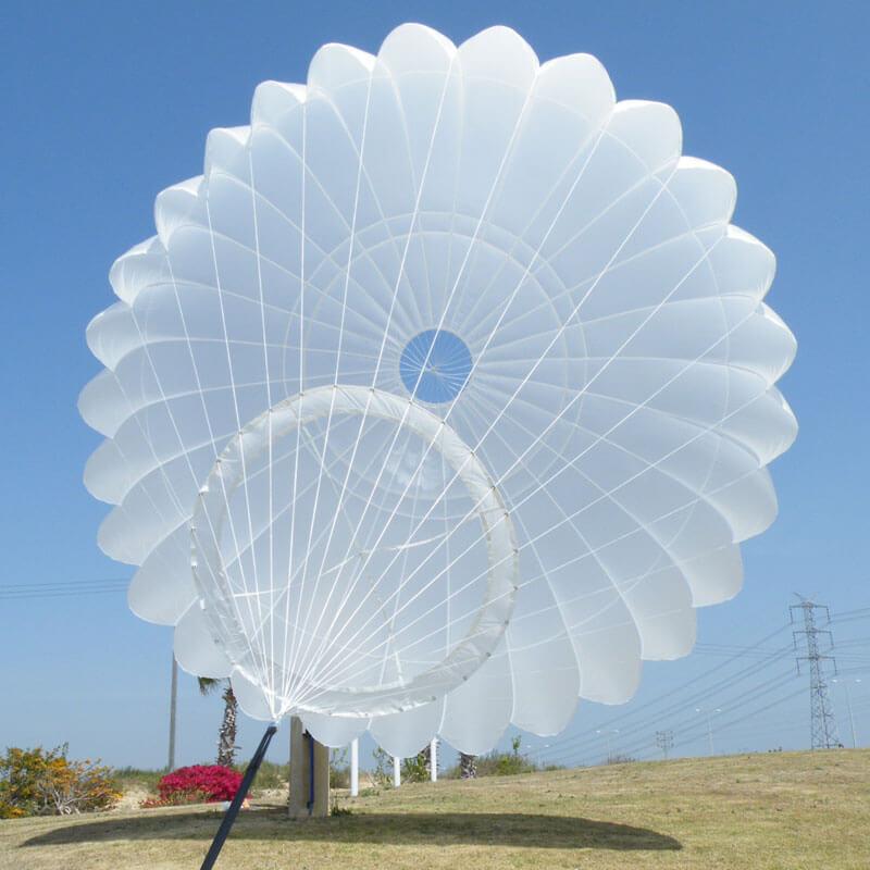 Campana redonda blanca con un panel intermedio que la rodea y las suspentes abriéndose en estrella, levantada en el suelo contra un cielo azul