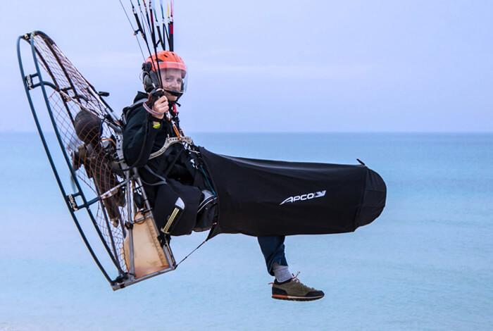 Piloto en un arnés motorizado sobre el mar, con una pierna aún estirada fuera del cocoon abierto