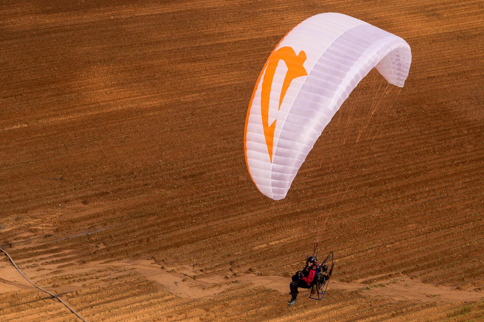 Piloto con una unidad motriz a la espalda volando bajo sobre tierras de labor recién aradas