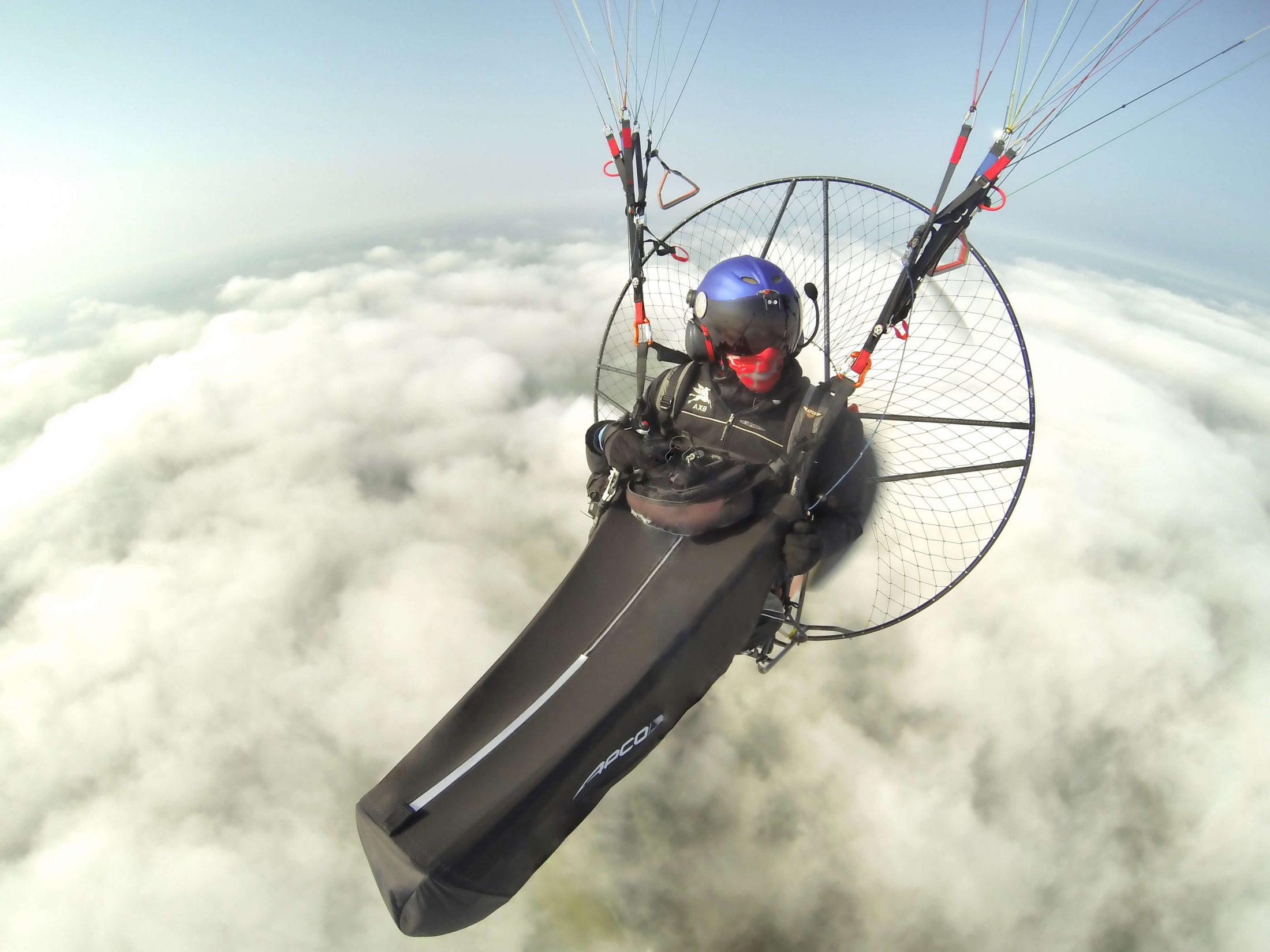 Vista frontal cercana de un piloto con casco, motor a la espalda y cocoon de piernas sobre una capa de nubes cerrada