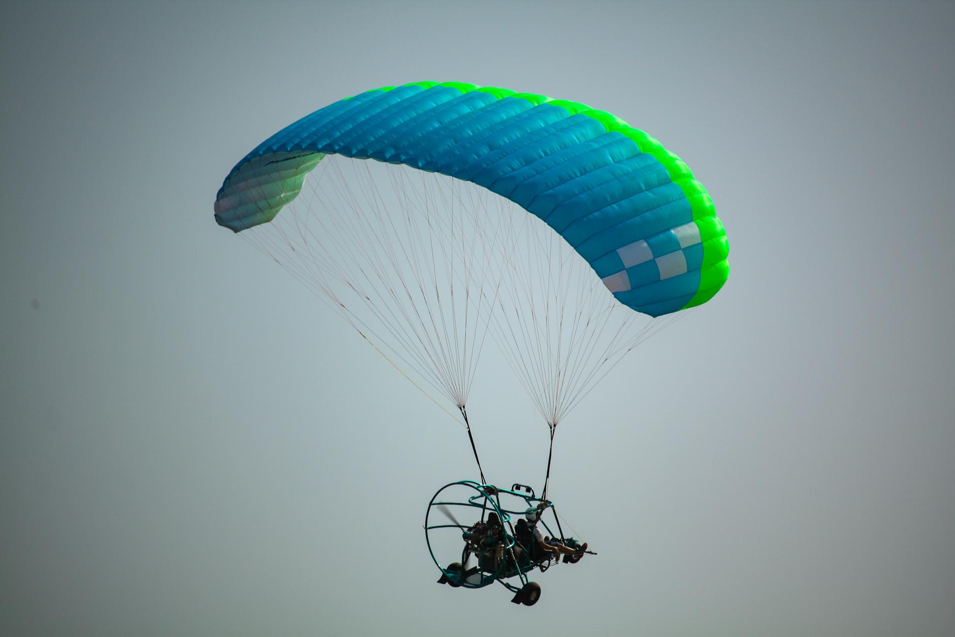 Trike biplaza con rueda de morro bajo una vela azul y verde, visto desde abajo contra el cielo