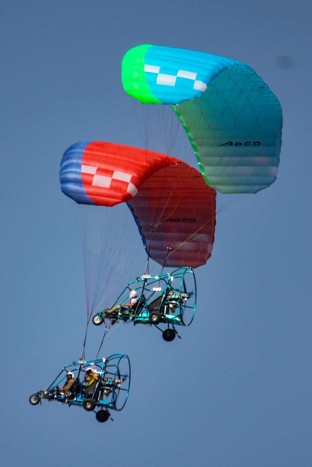 Dos trikes de construcción distinta volando en formación cerrada, uno sobre el otro, contra un cielo azul