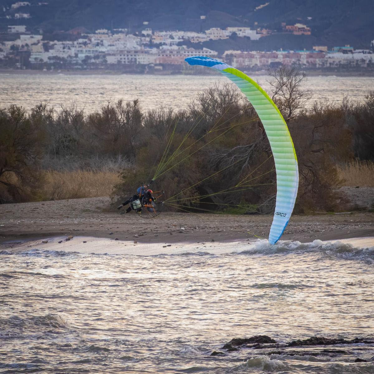 Velatura ram-air sollevata di taglio sopra la risacca mentre il pilota con il gruppo motore è inginocchiato sulla spiaggia